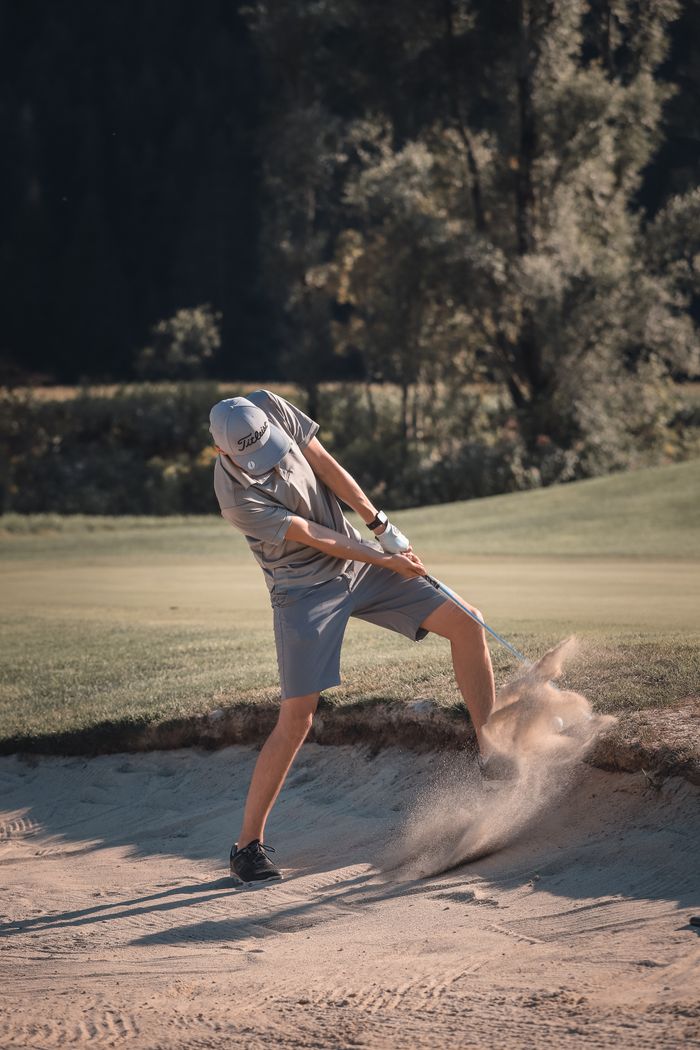 A golfer skillfully hits a shot from a sand bunker in a sunlit park in Lienz.