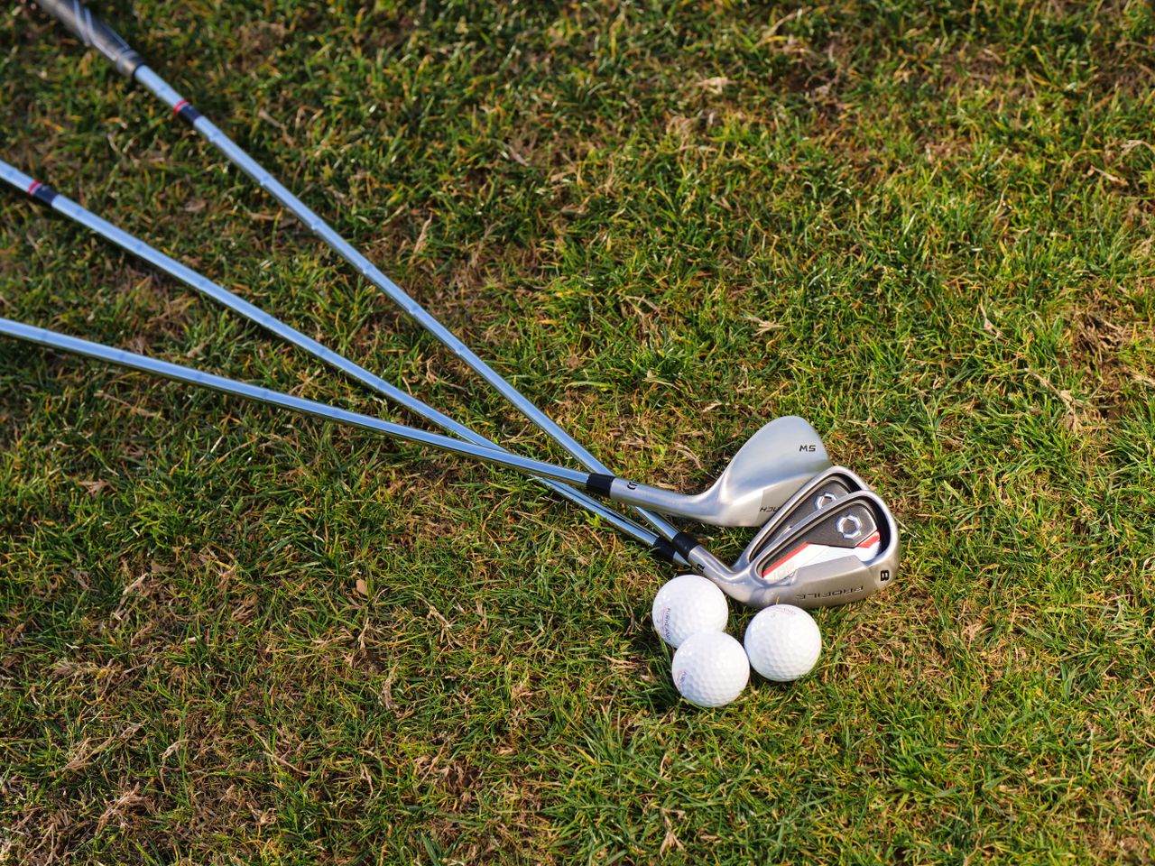 A set of golf irons with golf balls on a sunny grass field, perfect for golfing enthusiasts.