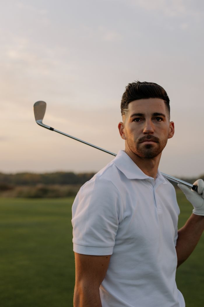 An adult male golfer posing with a club on a golf course at sunset, showcasing style and skill.